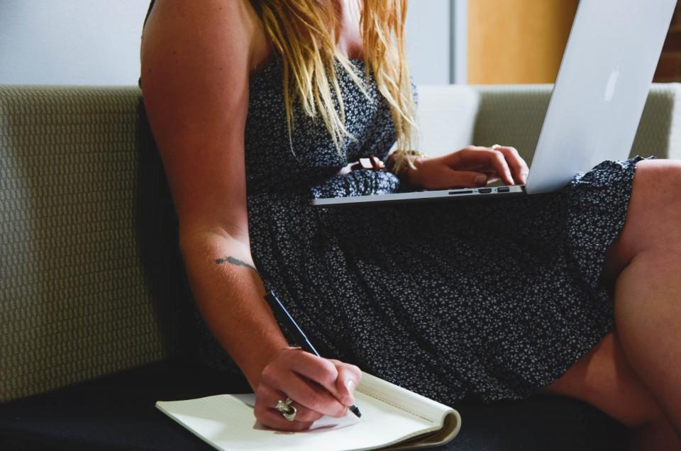Mulher estudando com notebook no colo e fazendo anotações em um caderno