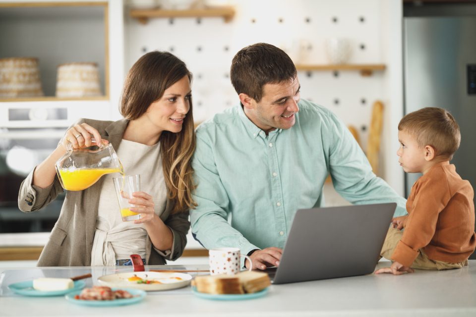 Família na cozinha enquanto um adulto trabalha no notebook na mesa compartilhada