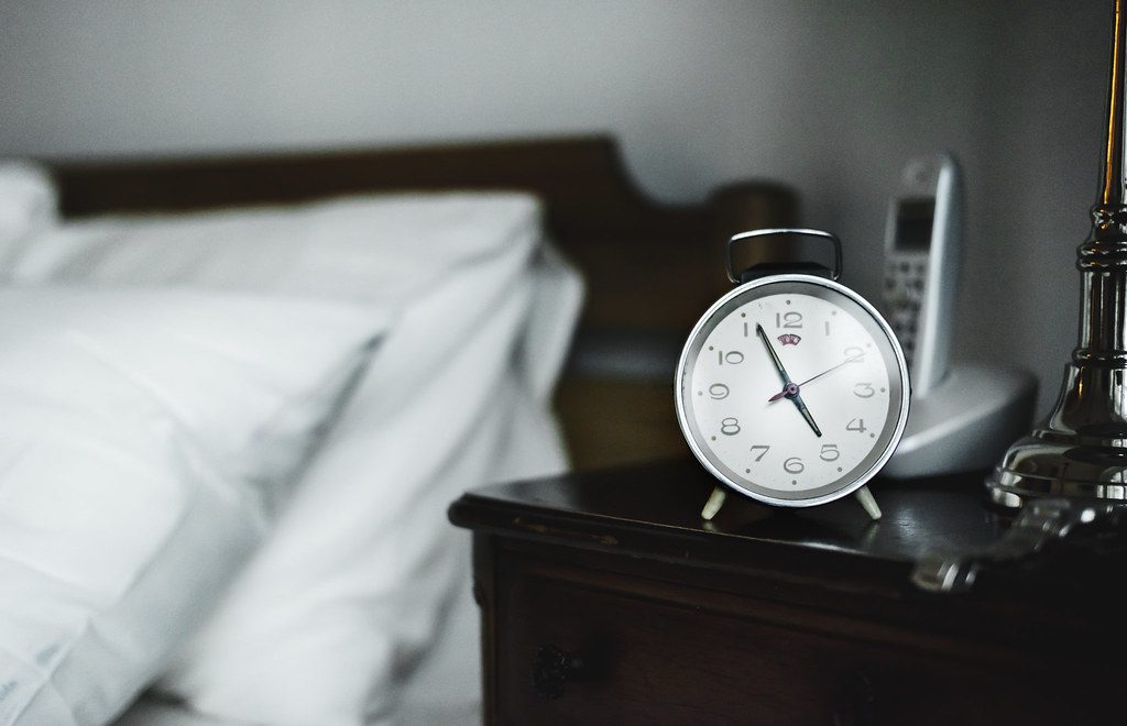 Despertador analógico no criado-mudo ao lado da cama pela manhã