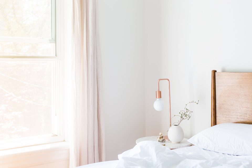 Quarto claro com cama arrumada e luz natural entrando pela janela de manhã
