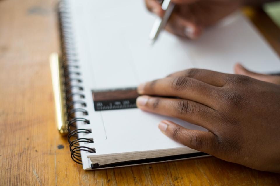 Estudante escrevendo em um caderno espiral sobre mesa de madeira