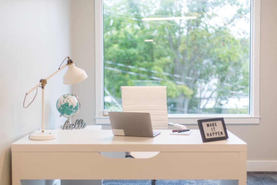 Mesa de home office com notebook e luminária ao lado de uma janela