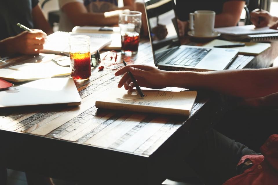 Mesa de reunião com cadernos, notebooks e bebidas durante uma conversa de trabalho