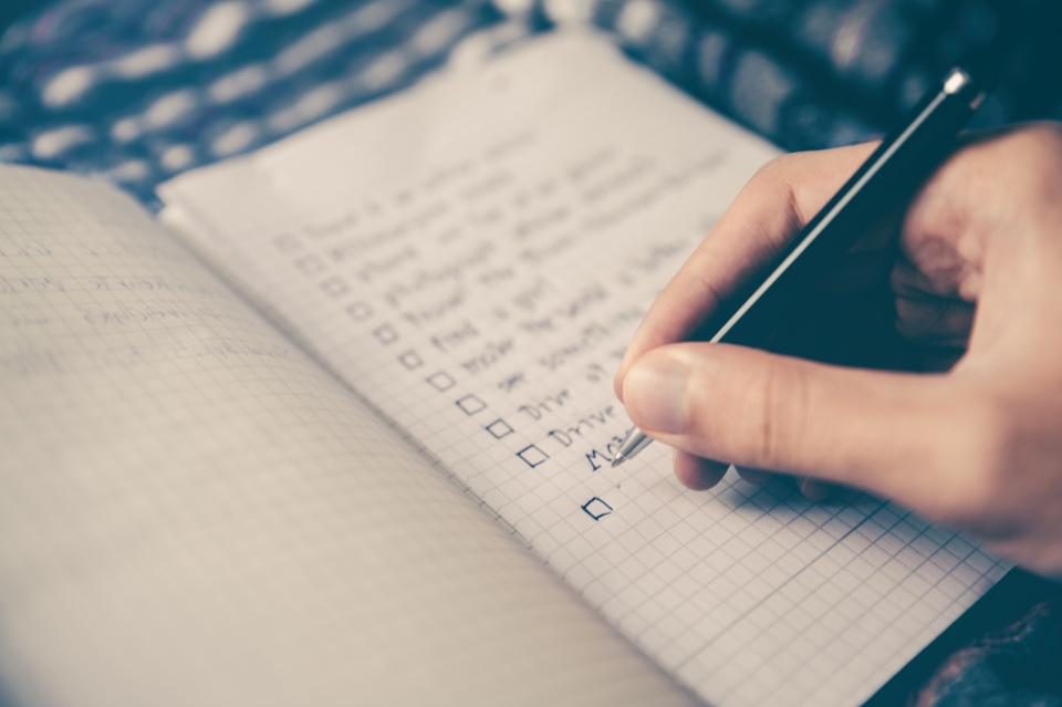 Mão marcando itens de uma lista de tarefas em um caderno